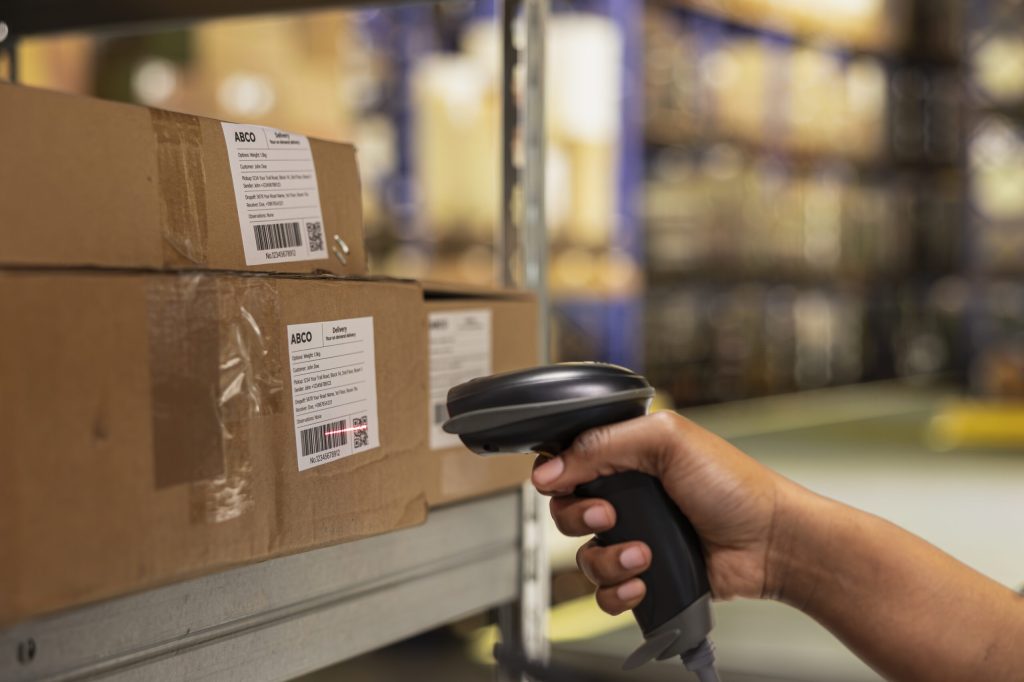 Close up of black woman worker scanning packages in a large storehouse, registering airway bills shipment details within industrial depot records. Using Philippines Top 5 Features of a Modern WMS scanner for order fulfillment.