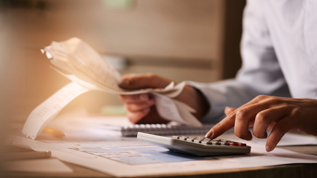 Close-up of economist using calculator while going through bills and taxes in the office.