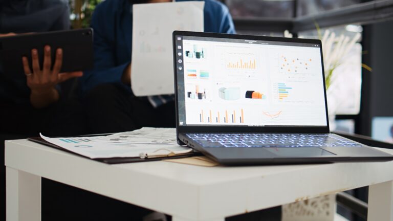 Two coworkers planning new strategy and analyzing online company information in startup office. Business partners collaborating on analytics presentation, using laptop and papers.